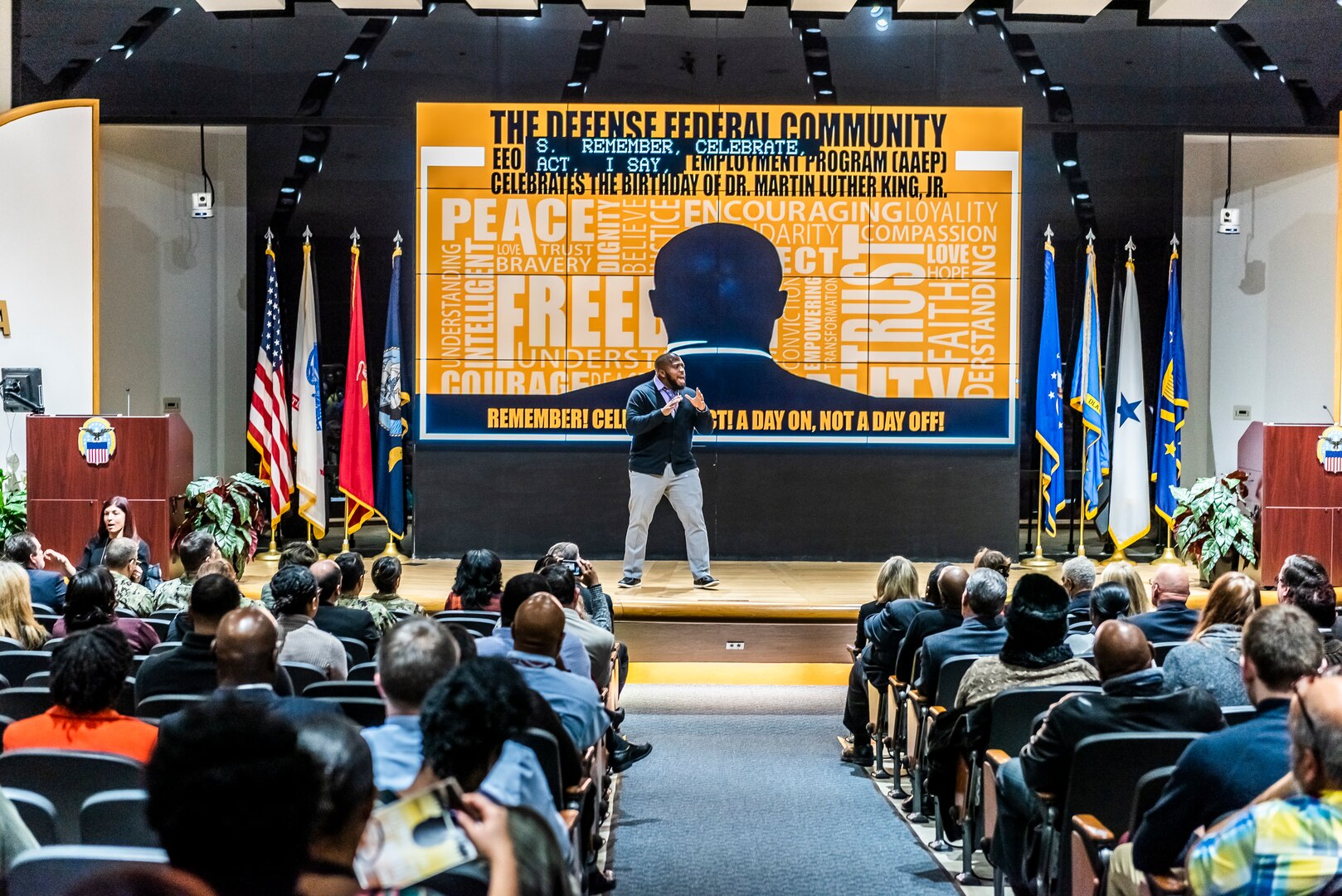 Associate stands on stage with a microphone in an auditorium full of people.