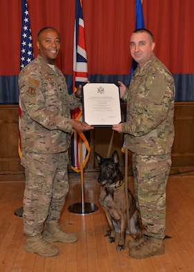 U.S. Air Force Lt. Col. Lawrence Wyatt, right, 100th Security Forces Squadron commander, shows the bite sleeve to Military Working Dog Vvonya, held by Tech. Sgt. Kelly Webster, 100th SFS MWD kennel master, for her last bite during her retirement ceremony at RAF Mildenhall, England, Jan. 18, 2019. Webster and his family have adopted Vvonya as she retires after nine years military service. (U.S. Air Force photo by Karen Abeyasekere)