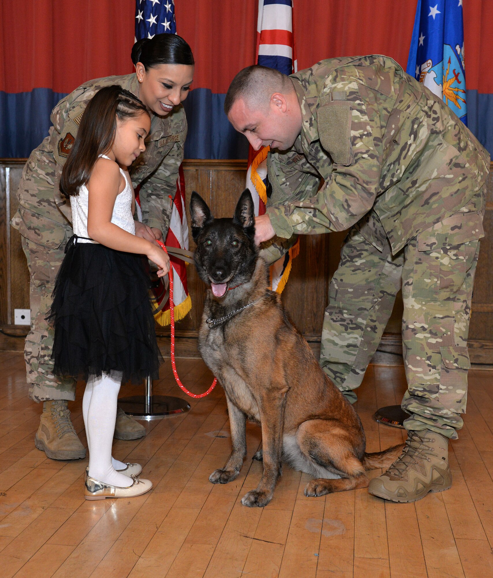 U.S. Air Force Tech. Sgt. Kelly Webster, right, 100th Security Forces Squadron Military Working Dog kennel master, and his wife Staff Sgt. Jacqueline Rosales, 100th SFS response force leader, and daughter Aubrey, put a new red, civilian collar on former MWD Vvonya at her retirement ceremony at RAF Mildenhall, England, Jan. 18, 2019. Webster and his family have adopted Vvonya as she retires after nine years military service. (U.S. Air Force photo by Karen Abeyasekere)