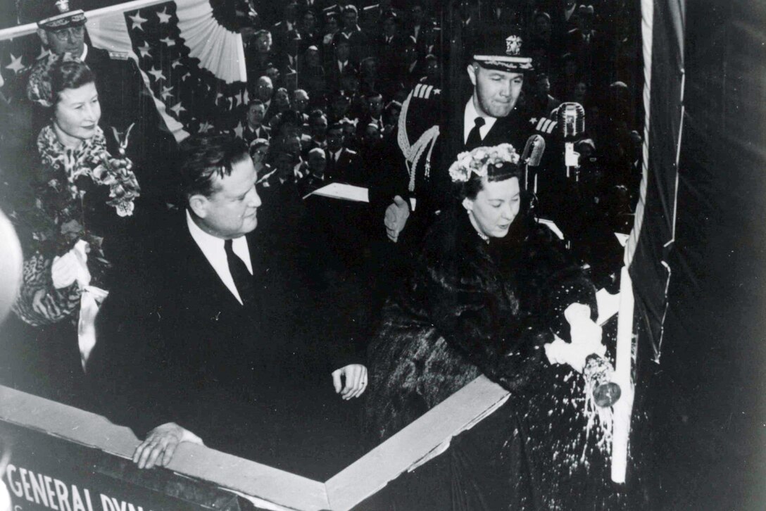 President Dwight D. Eisenhower stands next to his wife who is breaking a champagne bottle on a submarine.
