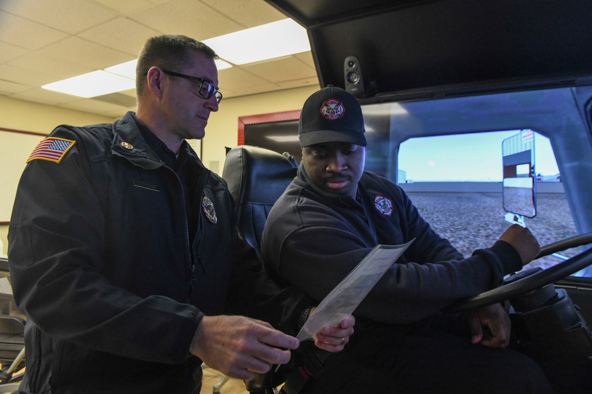 Philip Fourroux, the fire chief assigned to the 97th Air Mobility Wing Fire department, shows Jonathan Matthews, a firefighter assigned to the 97th AMW Fire Department, the directions to his destination before he operates a driving simulator, Jan. 15, 2019, at Altus Air Force Base, Okla. The simulator is one of three that allow the 97th AMW firefighters to train indoors on firefighting techniques, operating a water pump and driving various vehicles. (U.S. Air Force photo by Airman 1st Class Jeremy Wentworth)