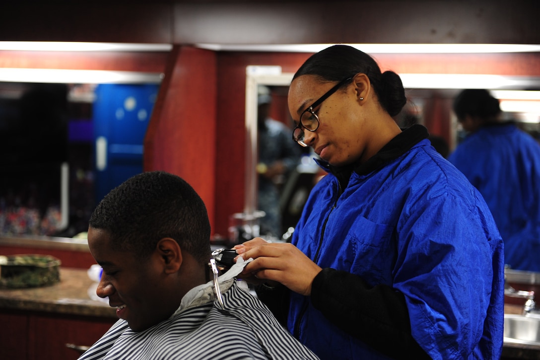 A sailor cuts the hair of another in a barber shop.