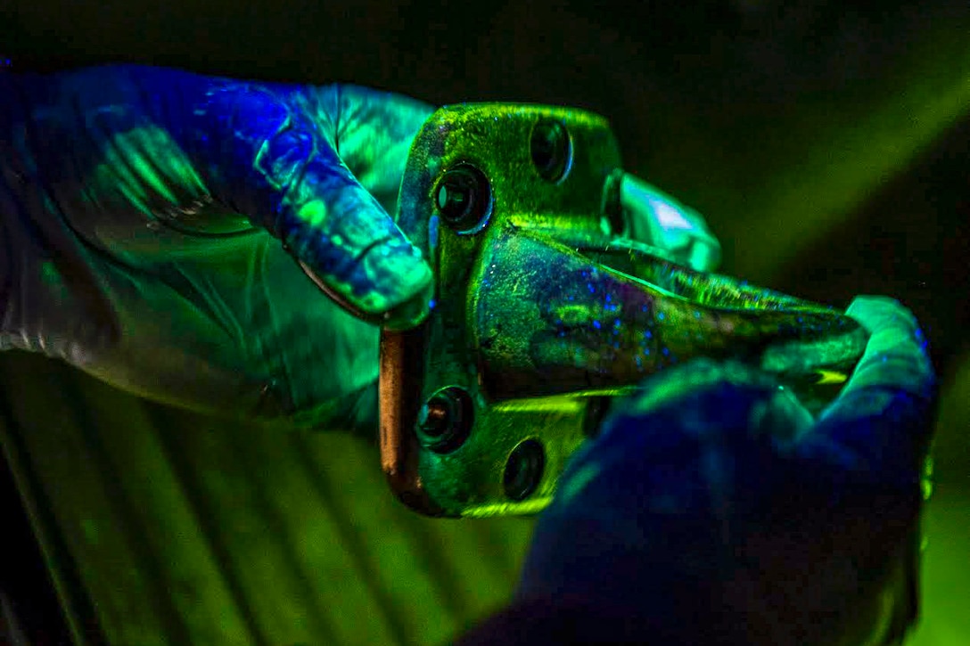 An airman looks at a piece of hardware under a blacklight.