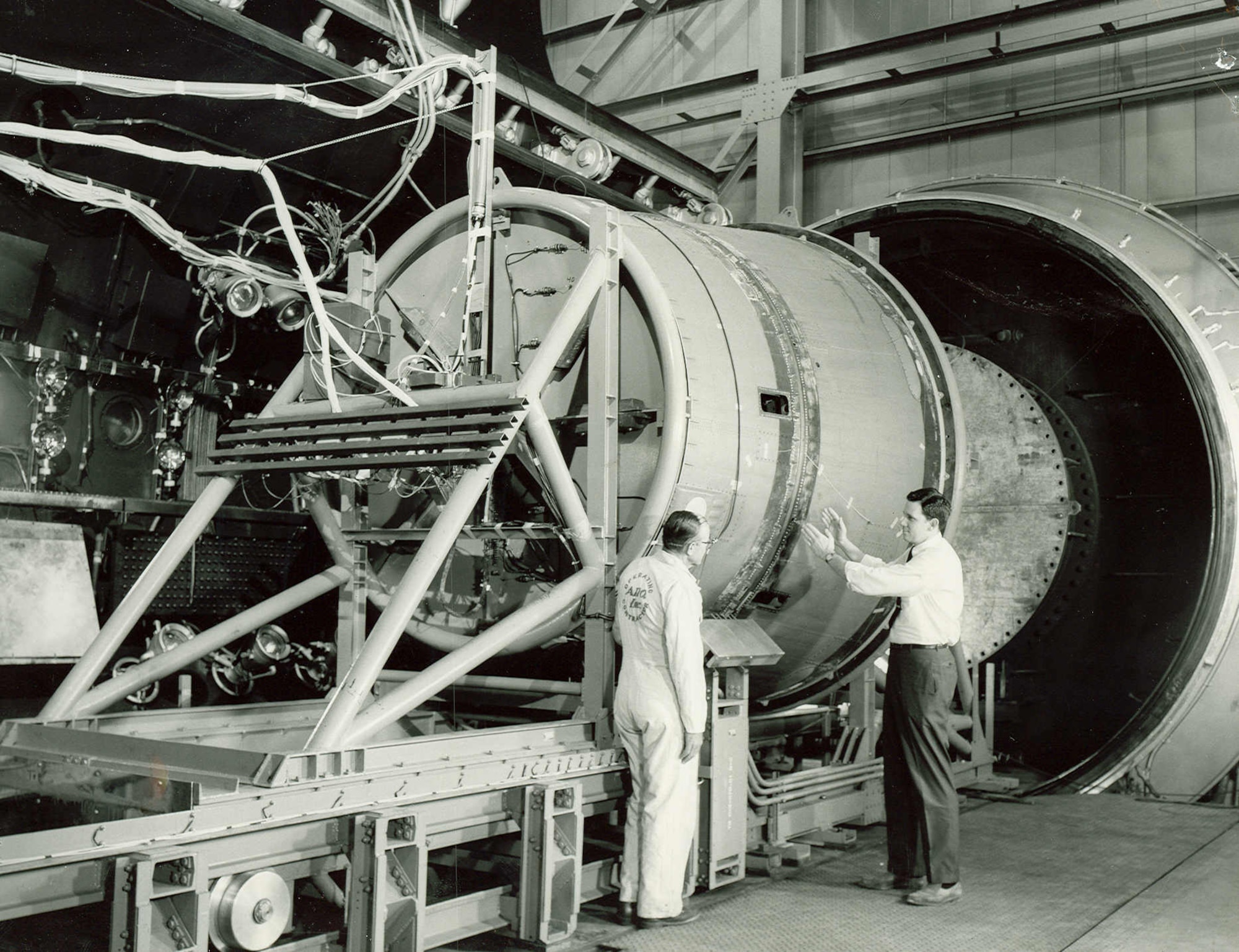 A full-scale replica of the Gemini adapter section and base of capsule is being prepared for simulated high altitude test of emergency abort system occurring in 1963 in the AEDC J-1 test cell at Arnold Air Force Base. The linear shaped explosive charge, which encircles the adapter section (the larger right-hand portion of this test installation), is set off to free the capsule from the booster, then the capsule retrorockets are fired to push the capsule away from the booster. The test showed modifications are needed to provide for successful emergency aborts. (U.S. Air Force photo)