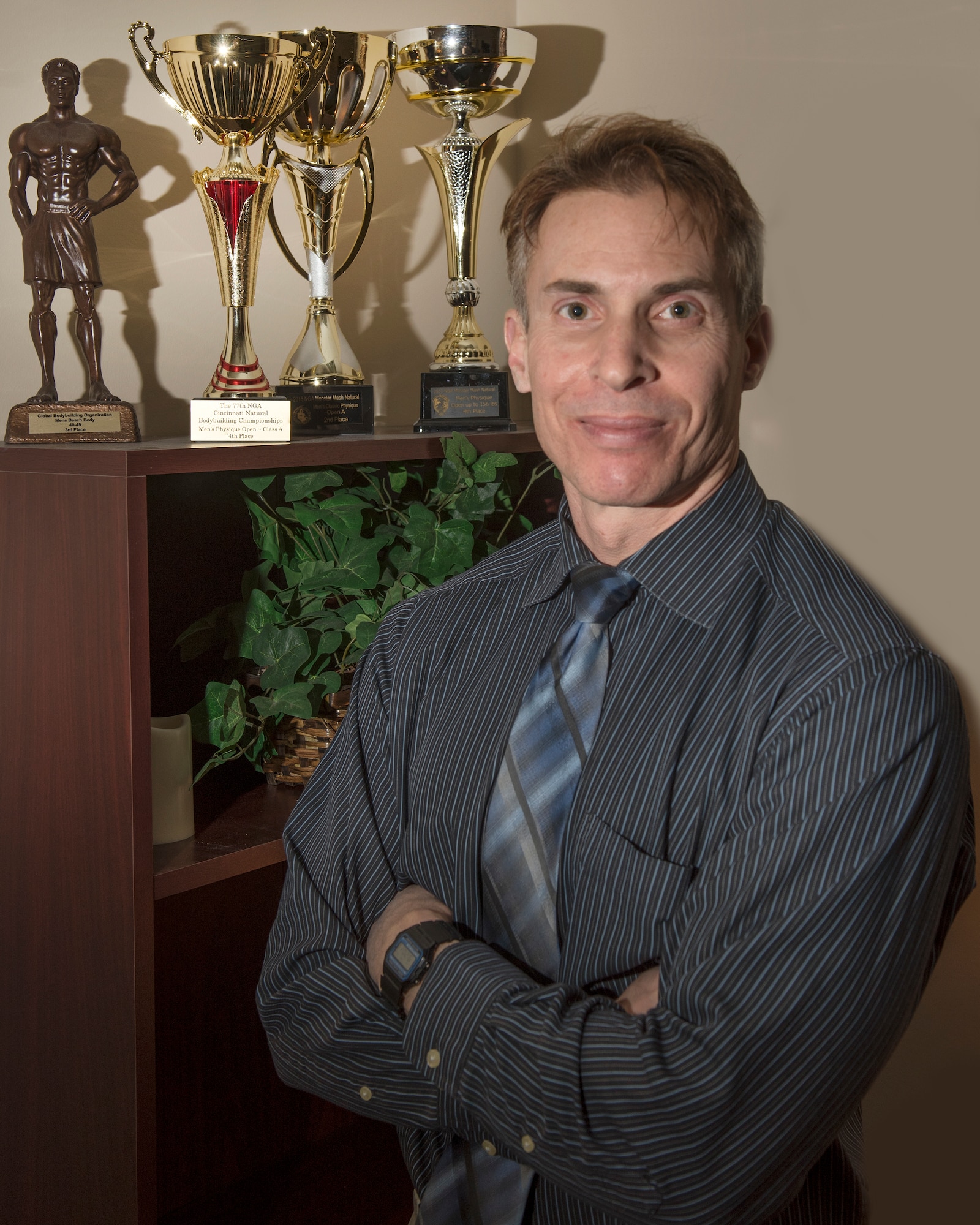 Eric Thayer, 88th Force Support Squadron Airman and Family Readiness flight chief, stands next to some of his many fitness awards inside his office at Wright-Patterson Air Force Base, Ohio, Jan. 10, 2019. Thayer has competed in several fitness competitions, such as for the Global Bodybuilding Organization and Cincinnati Natural Bodybuilding Championships. (U.S. Air Force photo by Michelle Gigante)