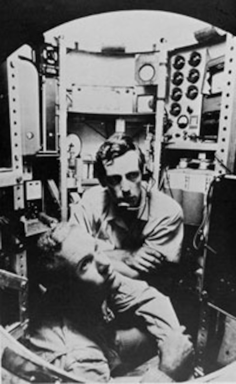 A black-and-white photo of two men in a submersible.