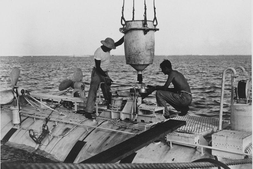 Two men load iron shot ballast into a submersible.