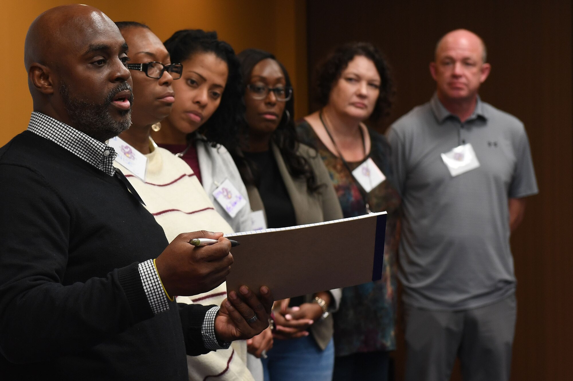 Six people stand up in the front of a room speaking.