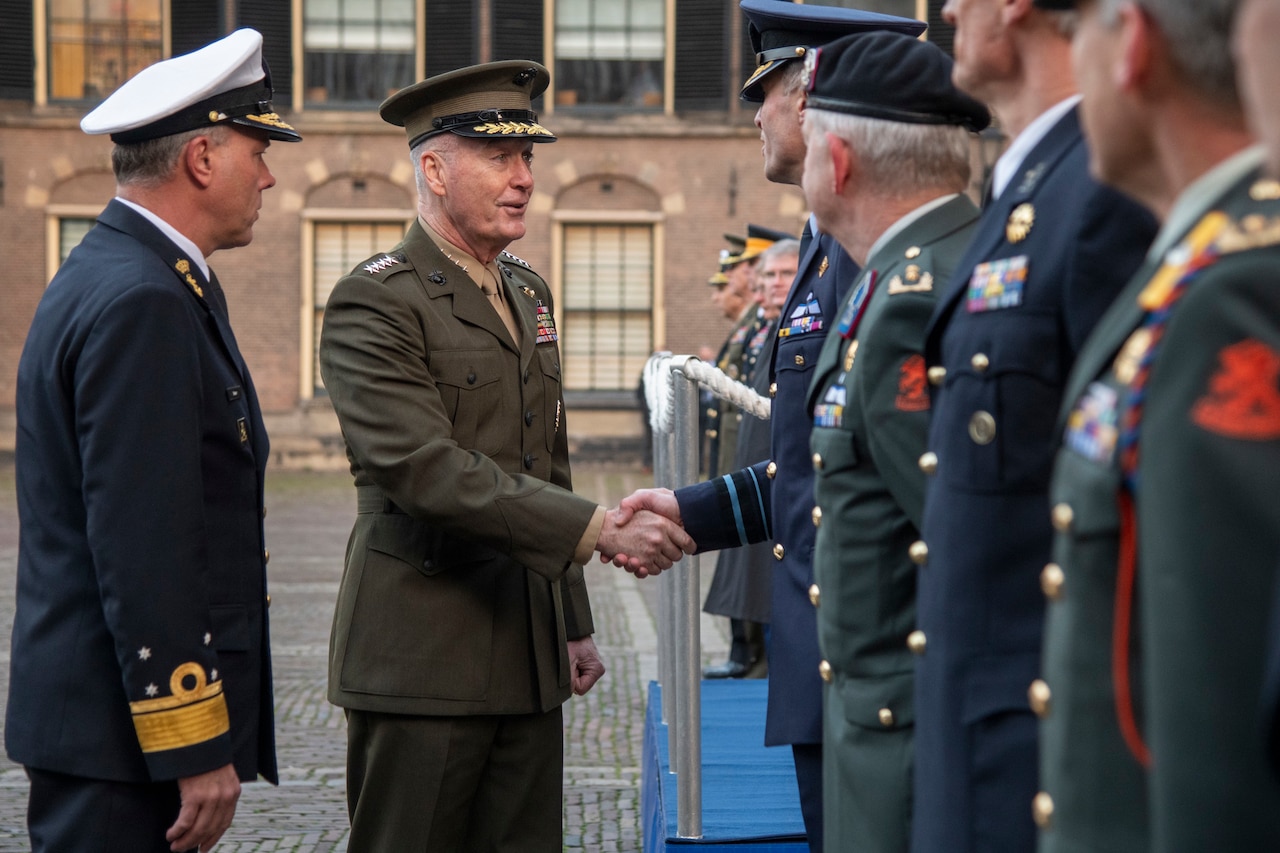 Joint Chiefs chairman shakes hands with a man standing with a group of other men.