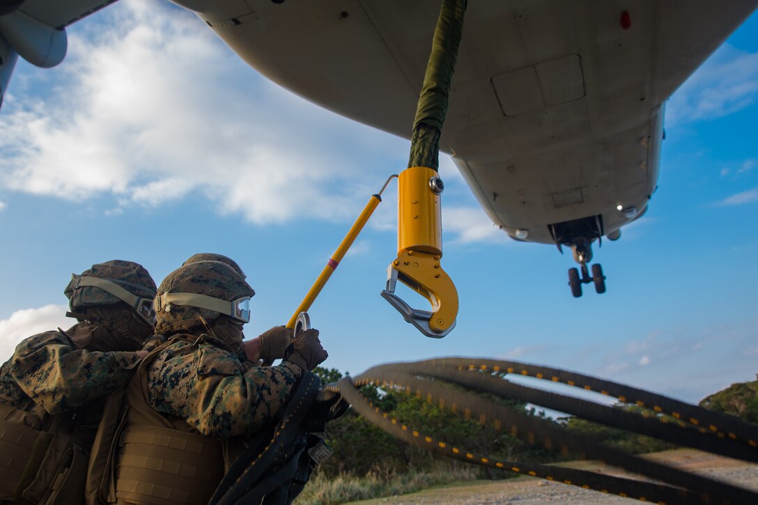 Landing support specialist attach an apex to an MV-22B Osprey hook during helicopter support team training at Camp Hansen, Okinawa, Japan, Jan. 14, 2019. Landing Support Company, 3rd Transportation Support Battalion, Combat Logistics Regiment 3, 3rd Marine Logistics Group supported Marine Medium Tiltrotor Squadron 265, Marine Aircraft Group 36, 1st Marine Aircraft Wing during external lift training, which ensures pilots and landing support specialists are able to communicate as well as transport gear from one location to another. (U.S. Marine Corps Photo by Cpl. André T. Peterson Jr.)