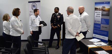 A soldier in dress blues surrounded by men and woman wearing white lab jackets while having a conversation