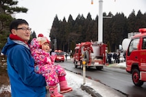 Misawa City Fire Department New Year ceremony attendants Ichika Kannoji and his daughter, Kiraki, watch fire trucks during a parade at Misawa City, Japan, Jan. 20, 2019. During the event, locals could spectate the fire drills and enjoy music played by the Misawa City Brass Band members. Misawa Air Base joins the local community in many New Year celebrations to take advantage of the cross-cultural opportunity. (U.S. Air Force photo by Senior Airman Sadie Colbert)