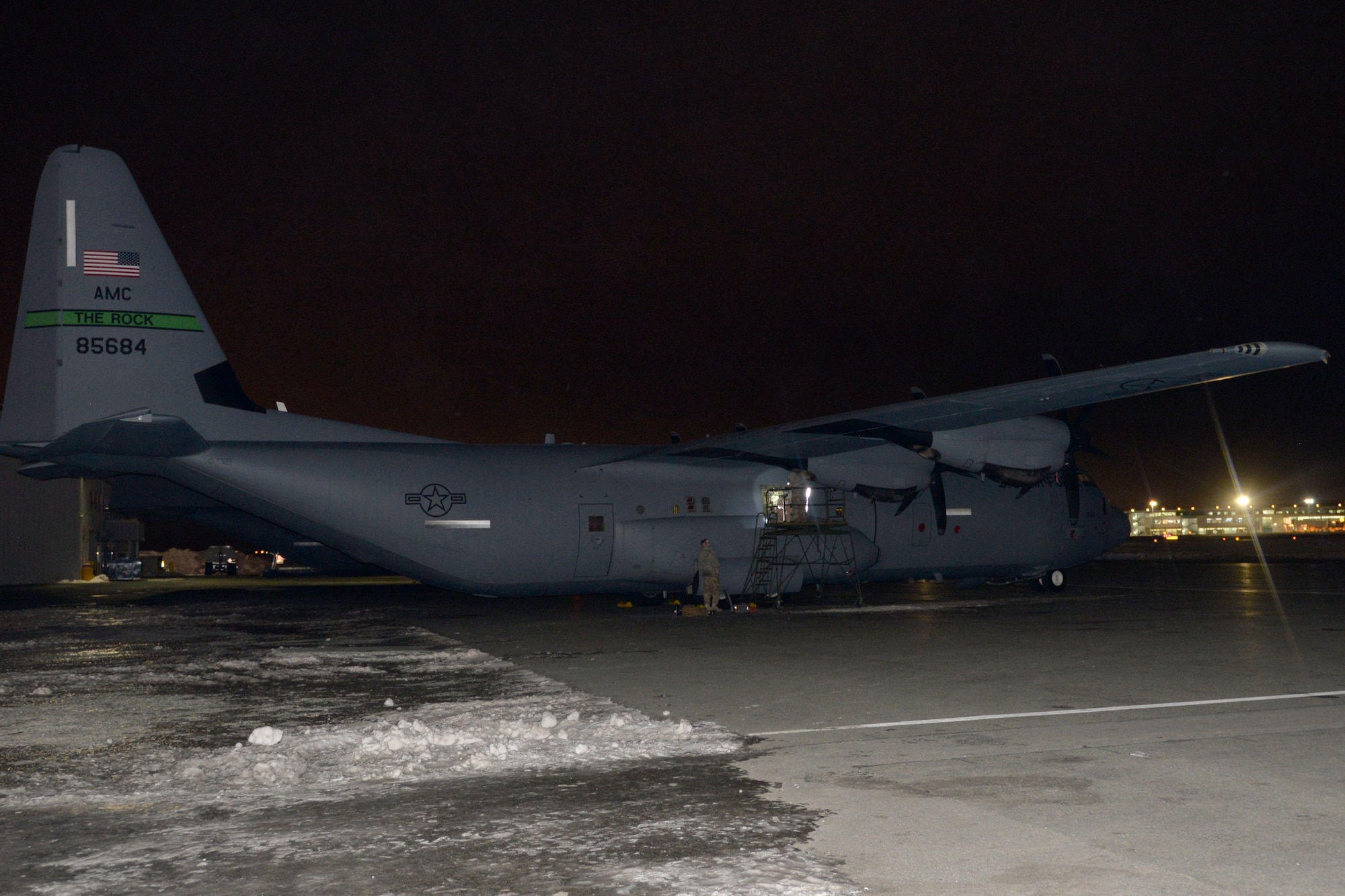 A C-130J in the dark surrounded by snow and ice.