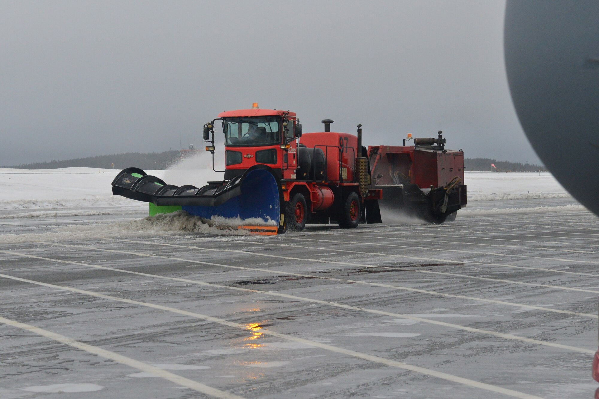 A plower plows ice and snow off a flightline.