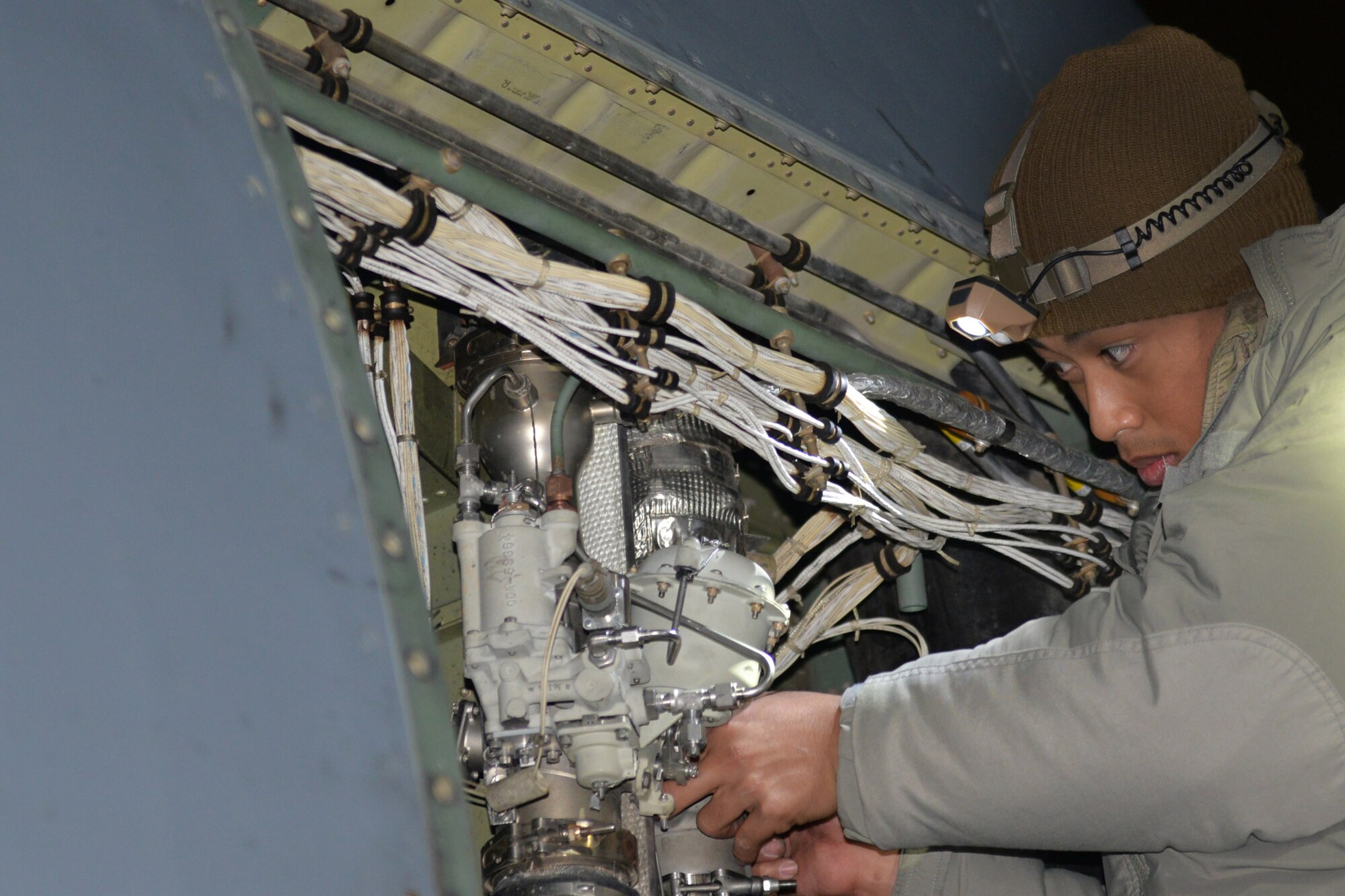 A man wearing a heavy winter coats fixes the inside of a C-130J.
