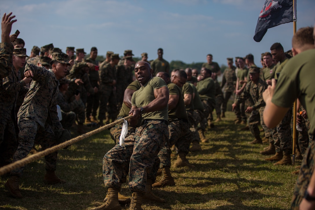 A group of Marines pull a rope surrounded by a crowd of Marines.