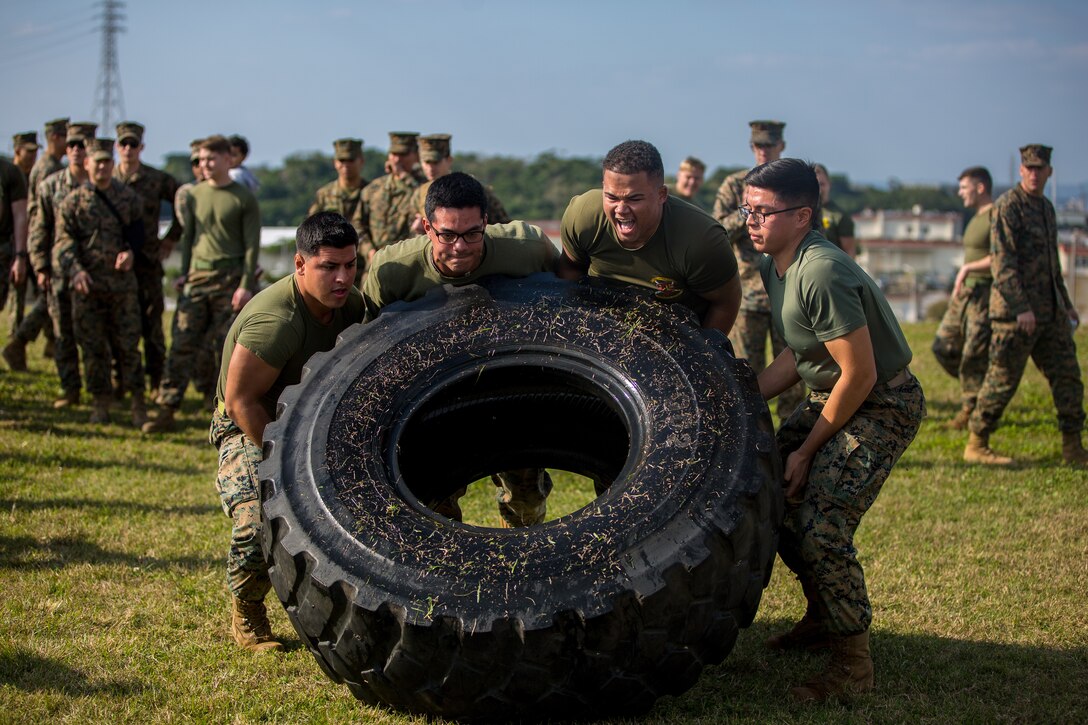Four Marines lift a tire while other Marines