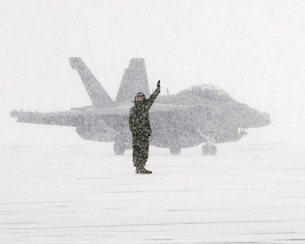 Sailor assigned to Electronic Attack Squadron (VAQ) 132 signals to E/A-18G Growler pilot as he taxis on flight line during snowstorm at Naval Air Facility Misawa, Japan, January 10, 2013 (U.S. Navy/Kenneth G. Takada)