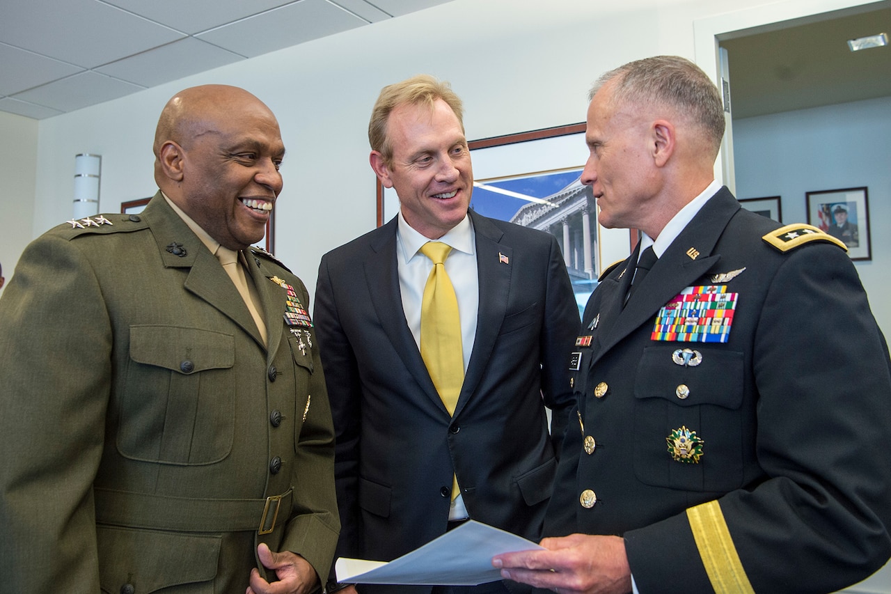 A Marine, a civilian and a soldier stand together in conversation.