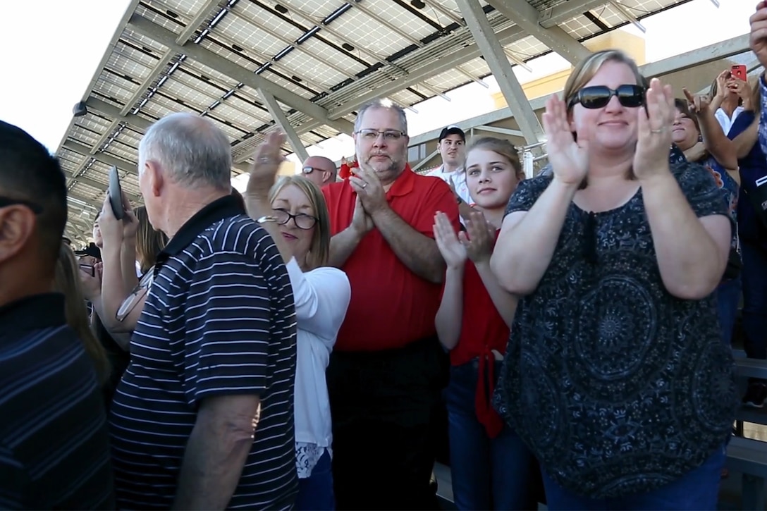 A crowd applauds while standing in metal bleachers.