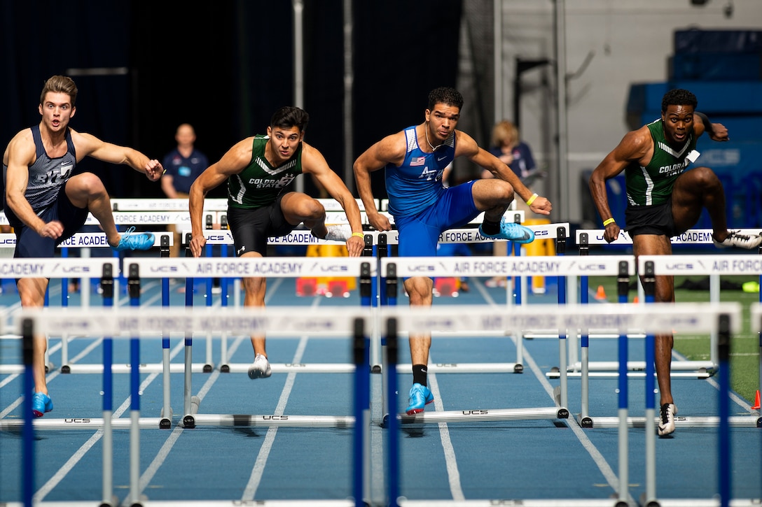 Four men jumping over hurdles on a track.