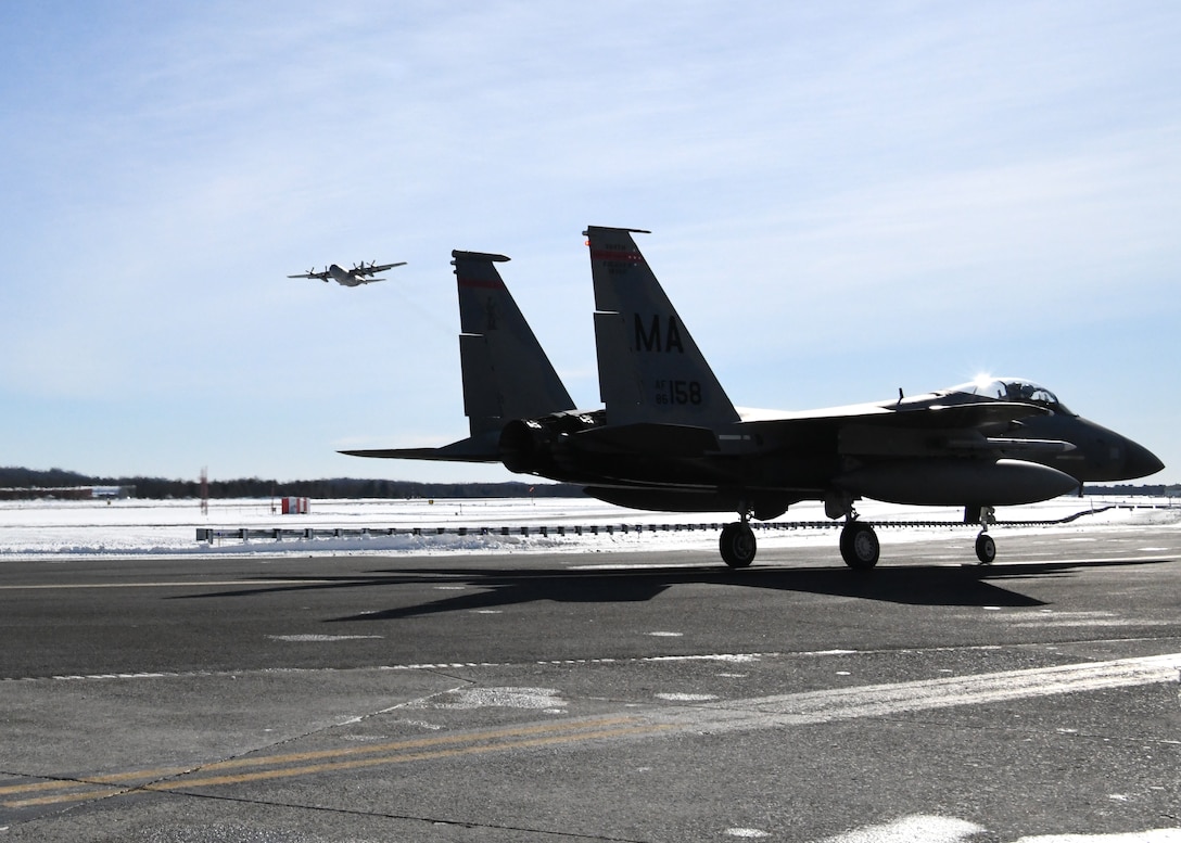 A C-130 Hercules from Bradley Air Force Base flies over a 104th Fighter Wing F-15 Jan. 22, 2019, at Barnes Air National Guard Base, Massachusetts. Airmen from the 104 FW aboard the C-130 depart for Patrick Air Force Base where they will train to help them prepare for various situations.  (U.S. Air National Guard photos by Airman Sara Kolinski)