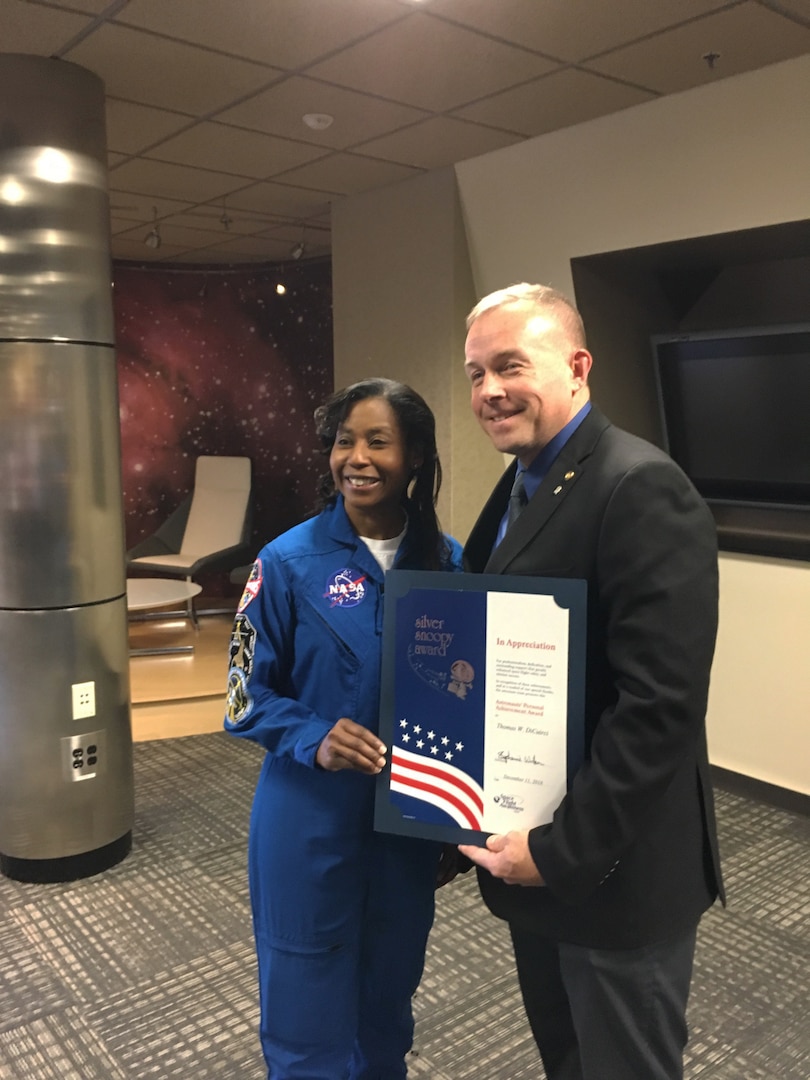 Female NASA astronaut presents a certificate to a male wearing a suit.