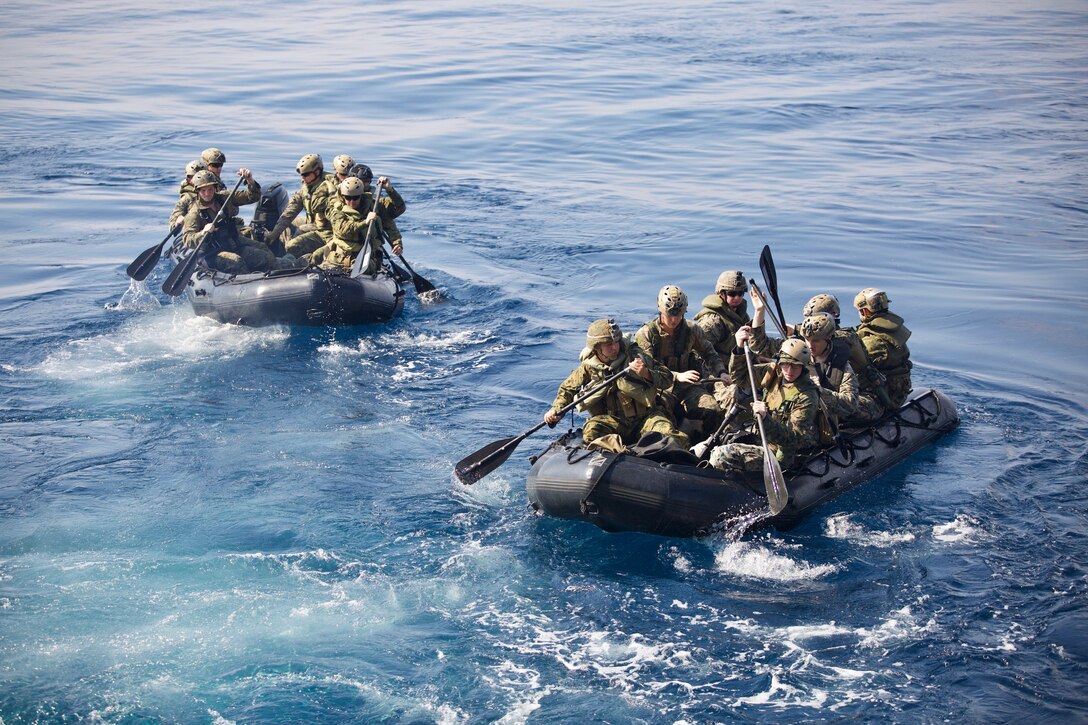 Marines in two rubber boats travel in blue waters.