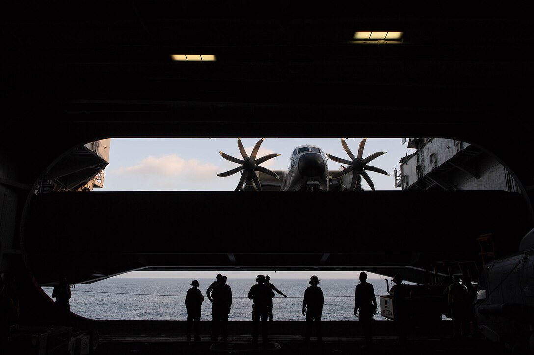 Sailors watch as a C-2A Greyhound aircraft is lowered on an aircraft elevator.