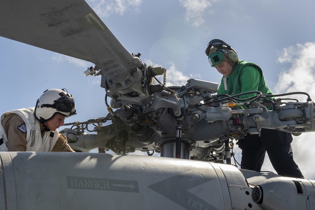 Service members perform preflight checks on a helicopter.