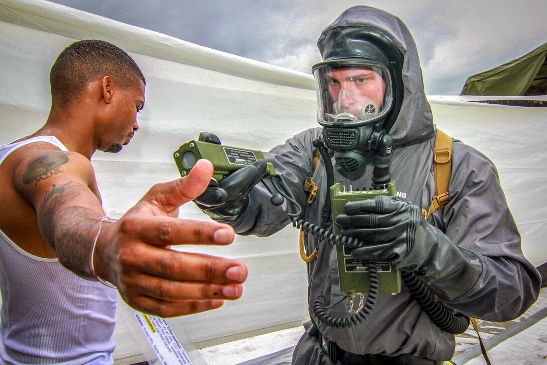 A soldier in a biohazard suit scans another soldier for contaminants.