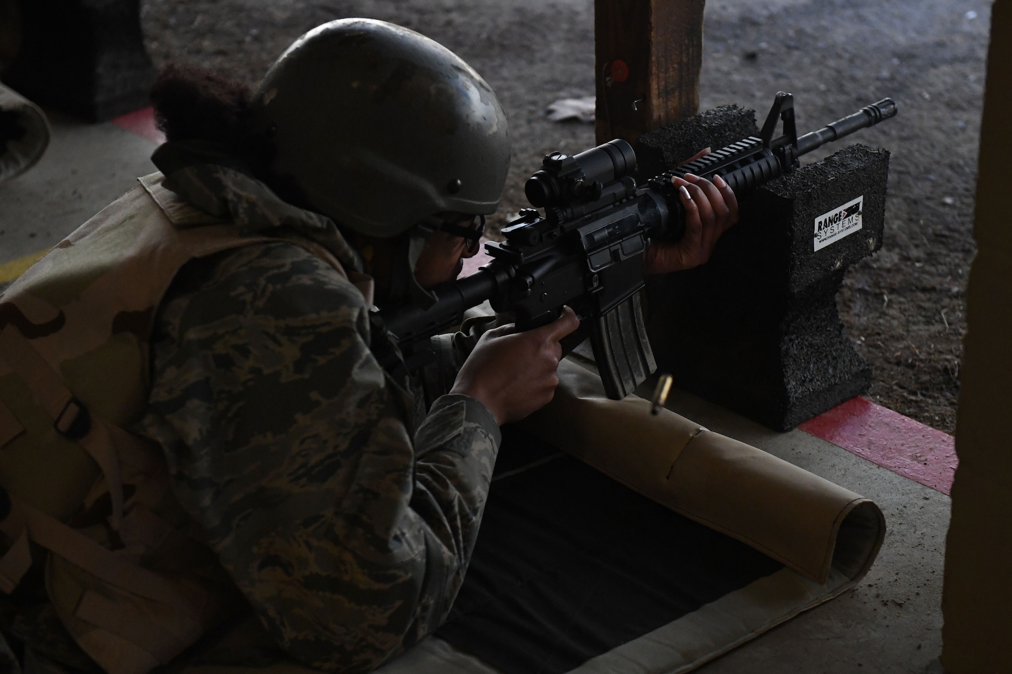 A woman lies on the ground and fires her rifle.