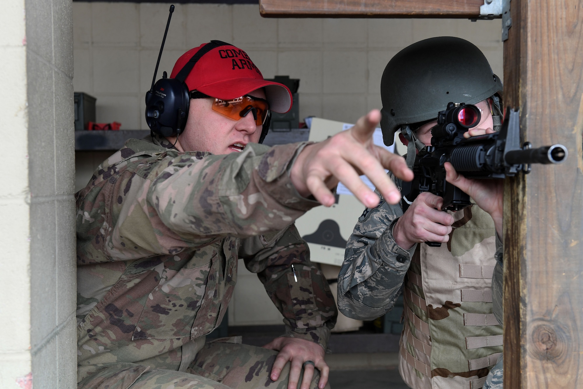 A man on the left of the photo points out of frame, while a man on the right of the photo aims his weapon in that direction.