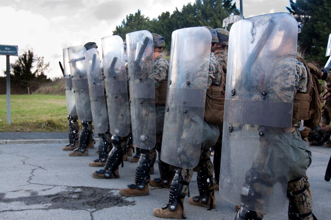 Marines stand in a line holding riot shields.