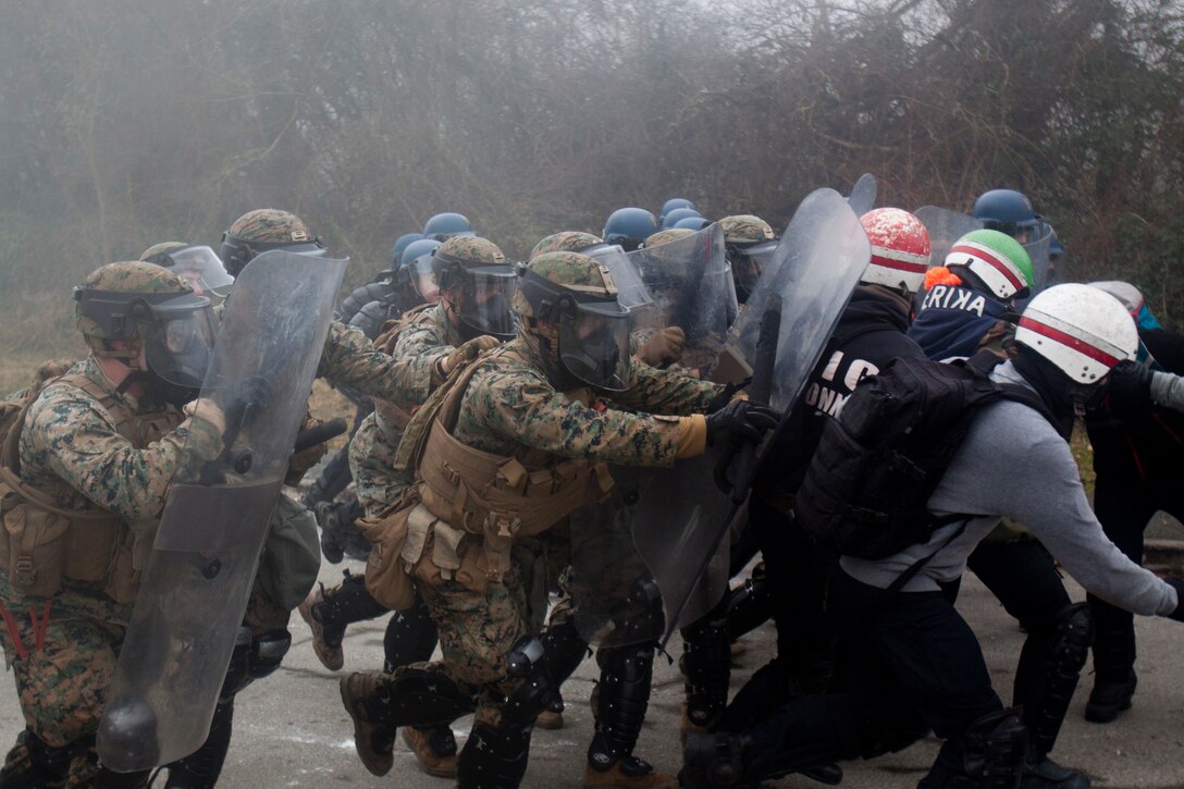 Marines and French gendarmes with riot shields push a line of role playing protestors.