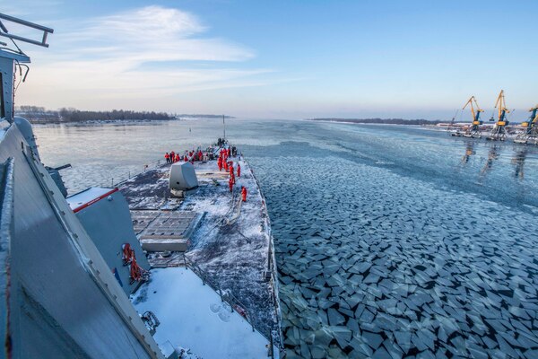 A boat traveling through icy waters with sailors on the deck.