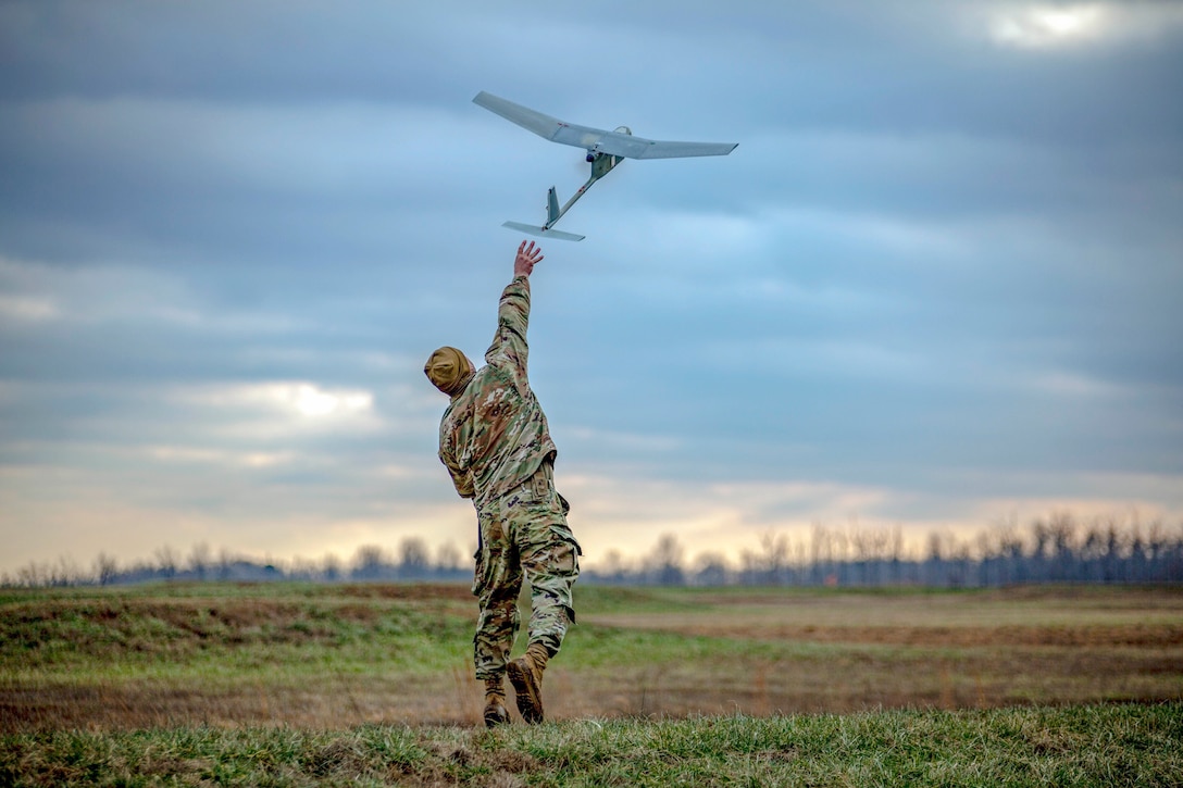 A soldier throws an unmanned aerial vehicle in a field.