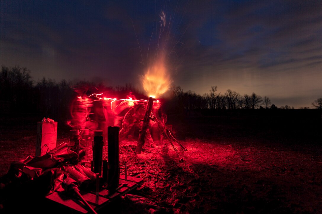 Soldiers fire a large weapon at night.