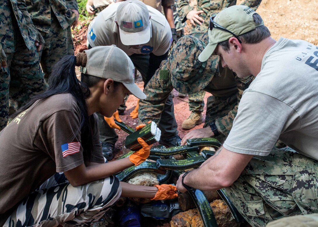 From left, Tiah Sengebau, a member with Norwegian Peoples Aid, a Palau Norwegian Peoples Aid member, U.S. Marine Corps Staff Sgt. Dent Hall, explosive ordnance disposal technician with Marine Wing Support Squadron 372, EOD 3 and U.S. Navy Explosive Ordnance Disposal 1st Class Charles Brown, with EOD Mobile Unit 5, Detachment Marianas, place Composition 4 explosives onto shell fragments during EOD training at a demolition range, Babeldaop, Republic of Palau, Nov. 28. TFKM Marines and Sailors deployed to conduct multilateral engagements designed to strengthen and enhance relationships among the U.S. and partner nations in the Indo-Pacific and South Pacific regions. (U.S. Marine Corps photo by Lance Cpl. Clare J. McIntire)