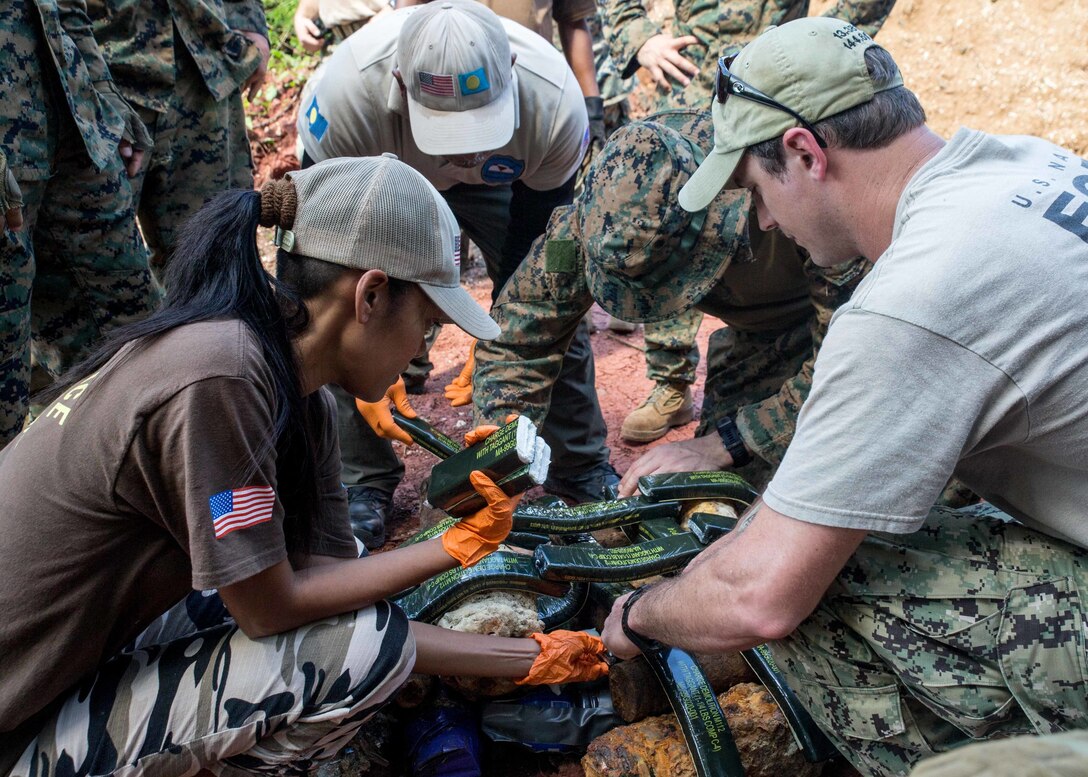 From left, Tiah Sengebau, a member with Norwegian Peoples Aid, a Palau Norwegian Peoples Aid member, U.S. Marine Corps Staff Sgt. Dent Hall, explosive ordnance disposal technician with Marine Wing Support Squadron 372, EOD 3 and U.S. Navy Explosive Ordnance Disposal 1st Class Charles Brown, with EOD Mobile Unit 5, Detachment Marianas, place Composition 4 explosives onto shell fragments during EOD training at a demolition range, Babeldaop, Republic of Palau, Nov. 28.