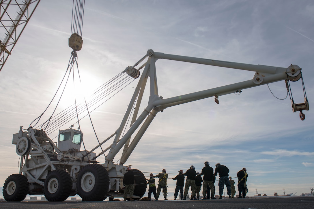 A group of sailors pull a large crane.