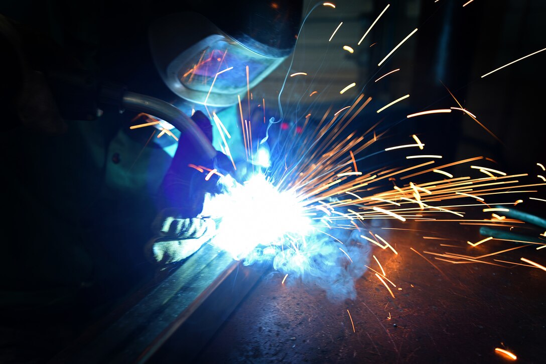 A service member welds a metal rod.