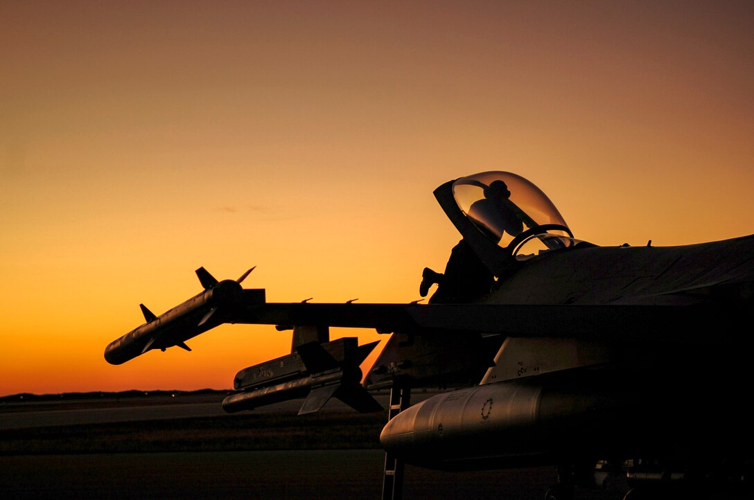 An Airman gets into a jet as the sun rises behind him.