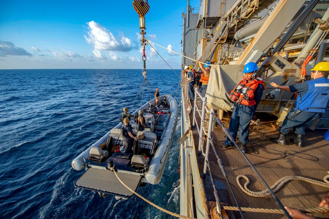 Sailors raise a boat into a Navy ship.