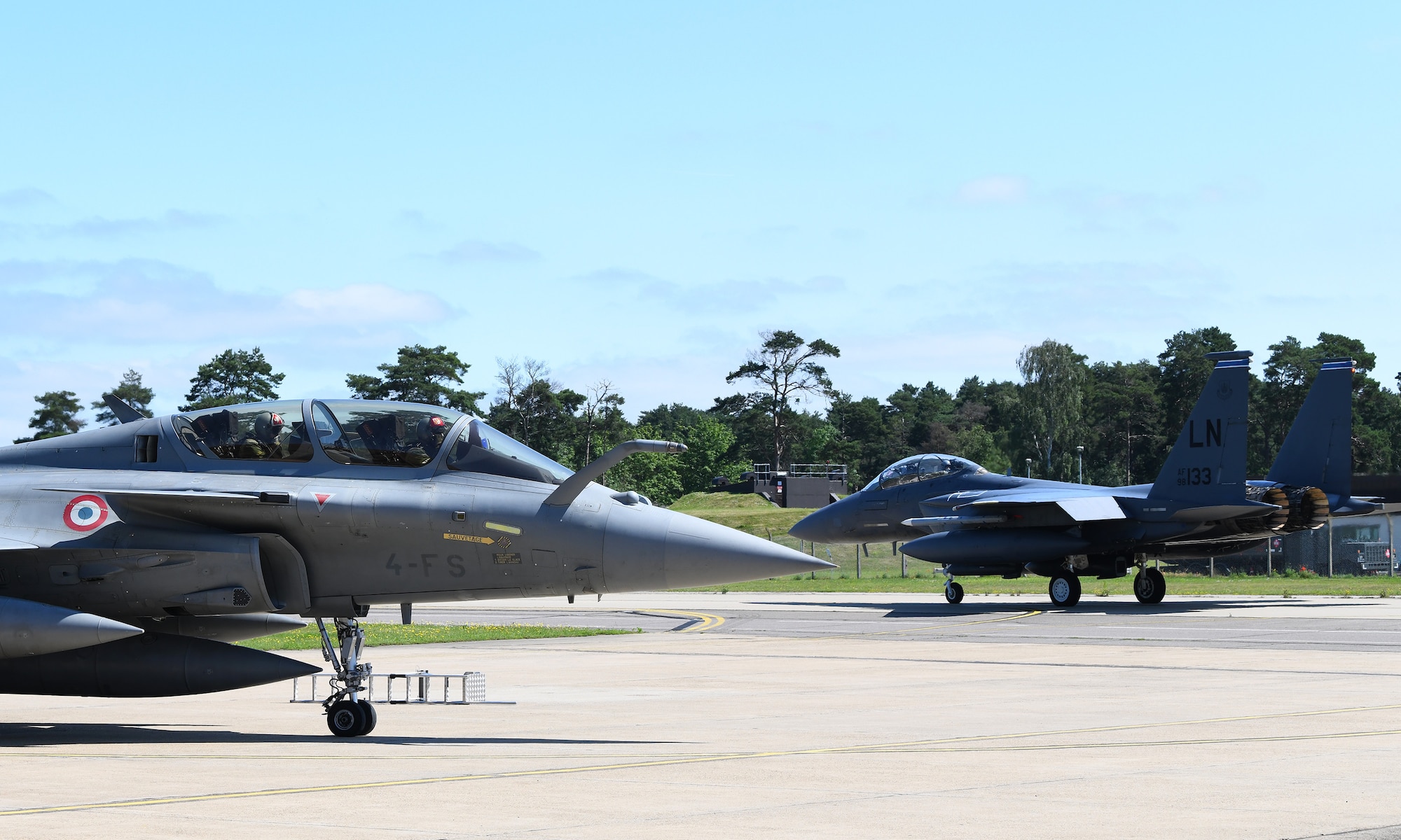 An F-15E Strike Eagle taxis past a French Air Force Rafale during exercise Point Blank 19-2 at Royal Air Force Lakenheath, England, June 17, 2019. More than 50 aircraft from three nations, U.S., France, and the UK, participated in the exercise promoting interoperability. (U.S. Air Force photo by Staff Sgt. Alex Fox Echols III/Released)