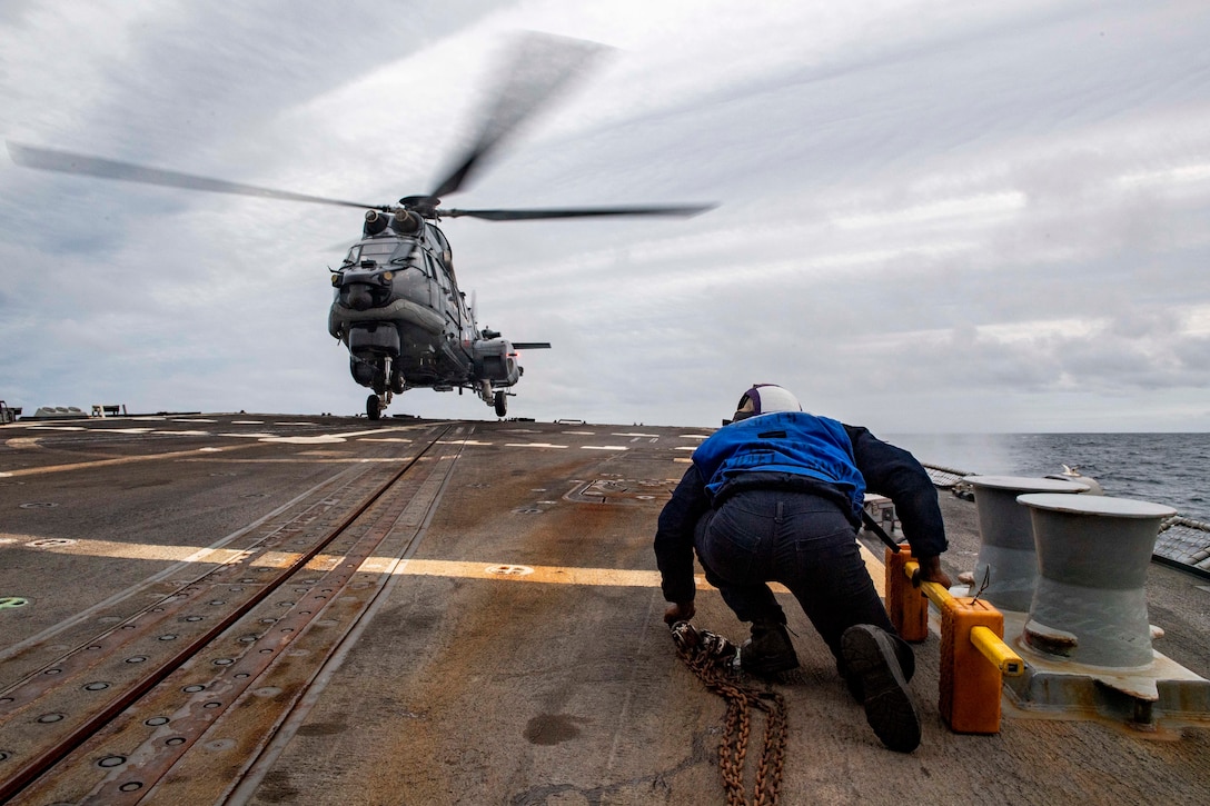 A U.S. Navy sailor prepares to chock and chain a helicopter.