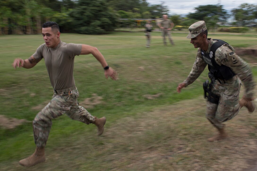 U.S. Army Spc. William Baez-Santos (left), 480th Military Police Company Forward 1 patrolman, chases down a simulated rioter during a joint training exercise June 26, 2019, at Soto Cano Air Base, Honduras. Members from Joint Task Force – Bravo’s Medical Element, 612th Air Base Squadron firefighters and 480th Military Police Company worked together to accomplish goals during the training event. The event involved the firefighters entering a smoke-filled building to recover burn casualties while the Medical Element performed triage at the scene. The 480TH MPC members provided a cordon of the area and kept rioting personnel from entering the scene. (U.S. Air Force photo by Staff Sgt. Eric Summers Jr.)