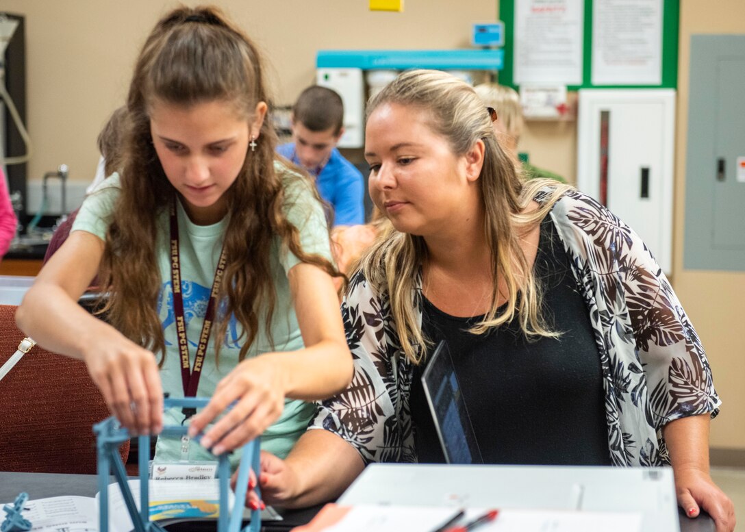 Nicole Waters, Fabrication and Prototype Shops Project Manager at the Naval Surface Warfare Center Panama City Division, assists students in the Civil Engineering course learn how to build model truss bridges. Students built these structures to withstand various applied forces in tension and compression and were required to repair any problems found once examined by Master Teachers.