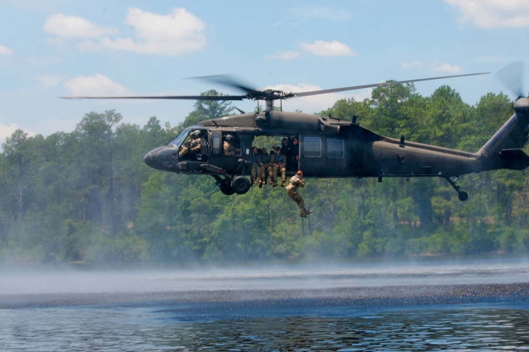 A soldier jumps out of a helicopter over water.