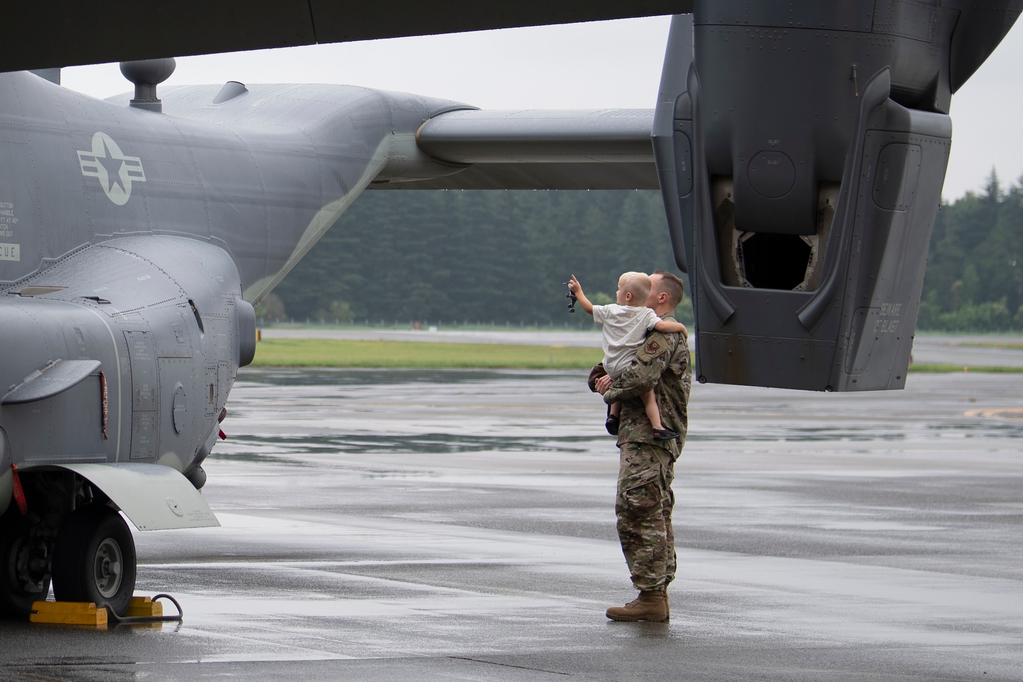 An Airman from Team Yokota looks at a CV-22 Osprey with his child during the assumption of command ceremony at Yokota Air Base, Japan, July 1, 2019.